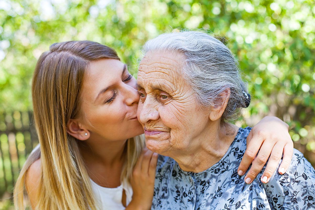 Frau küsst Seniorin auf die Wange